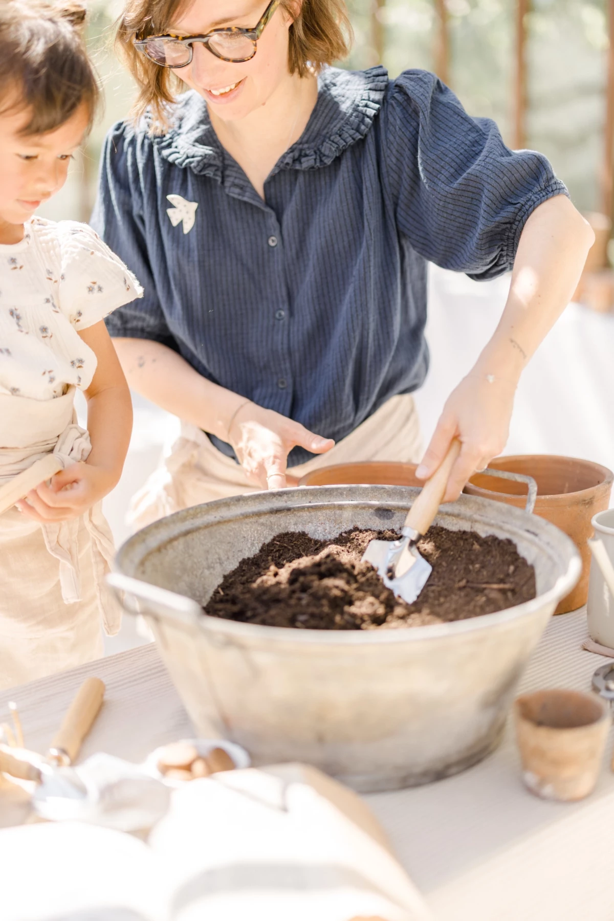 Séance famille au printemps : mère et fille partagent un moment complice lors d'un atelier jardinage dans une serre lumineuse