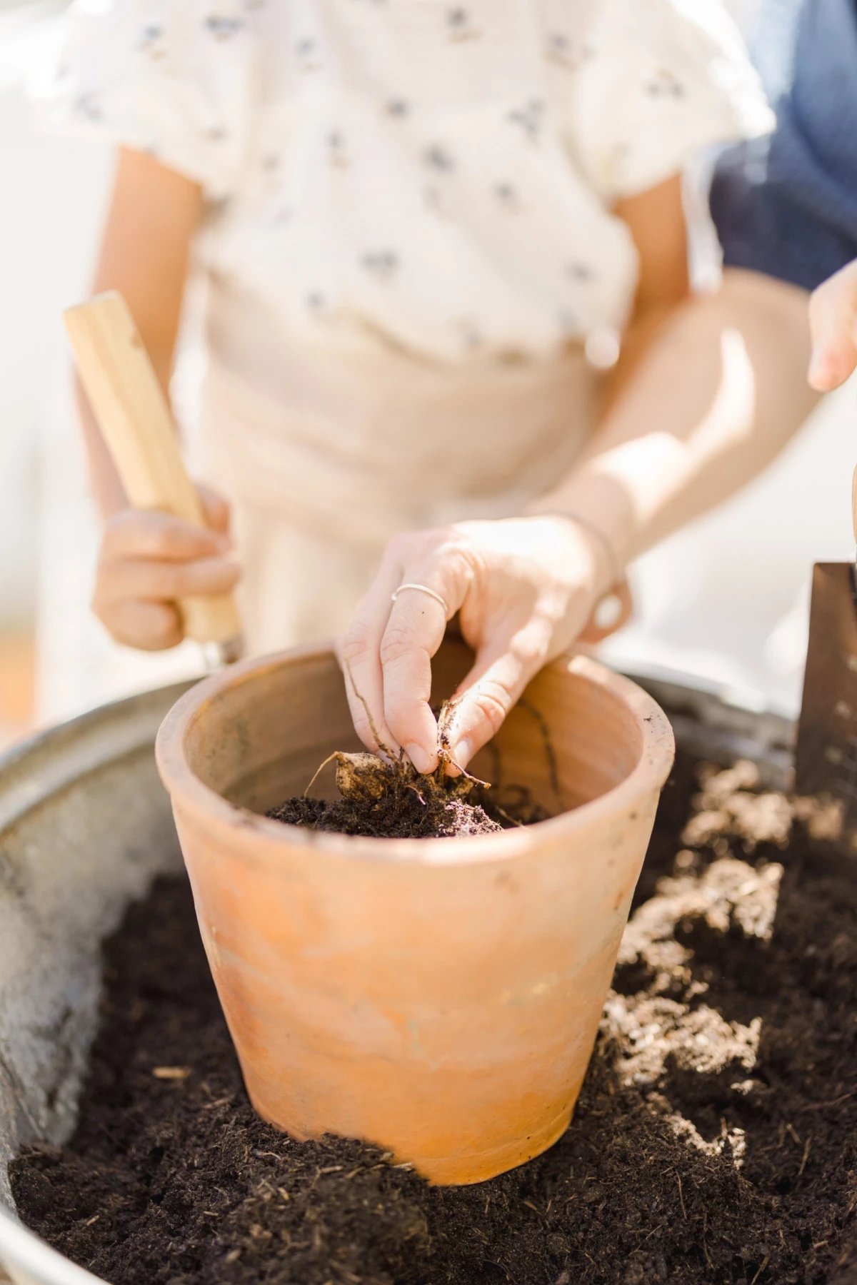 Séance famille jardinage : enfant plante une graine dans un pot en terre cuite, instant de complicité mère-fille au printemps