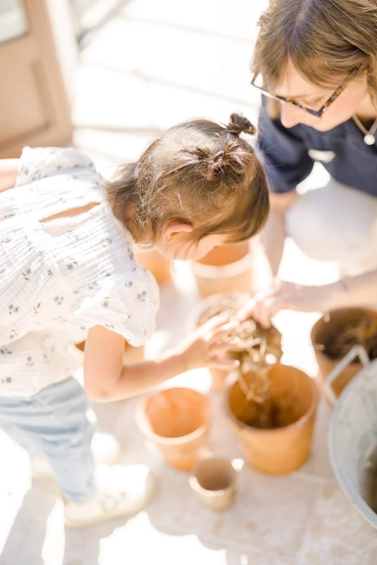 Séance famille printemps : mère et fille partagent un atelier jardinage dans une verrière lumineuse, complicité et nature