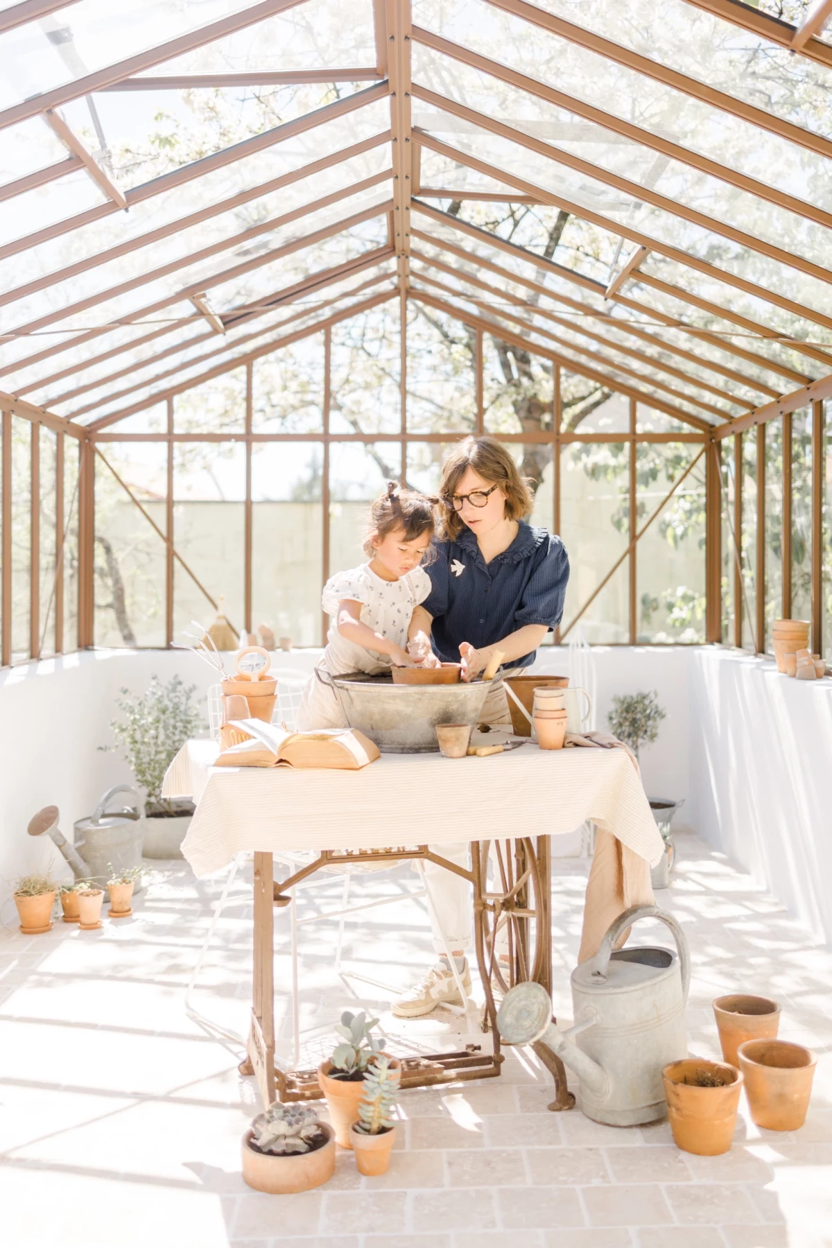 Séance famille printemps : mère et fille partagent un atelier jardinage dans une verrière lumineuse, moment de complicité
