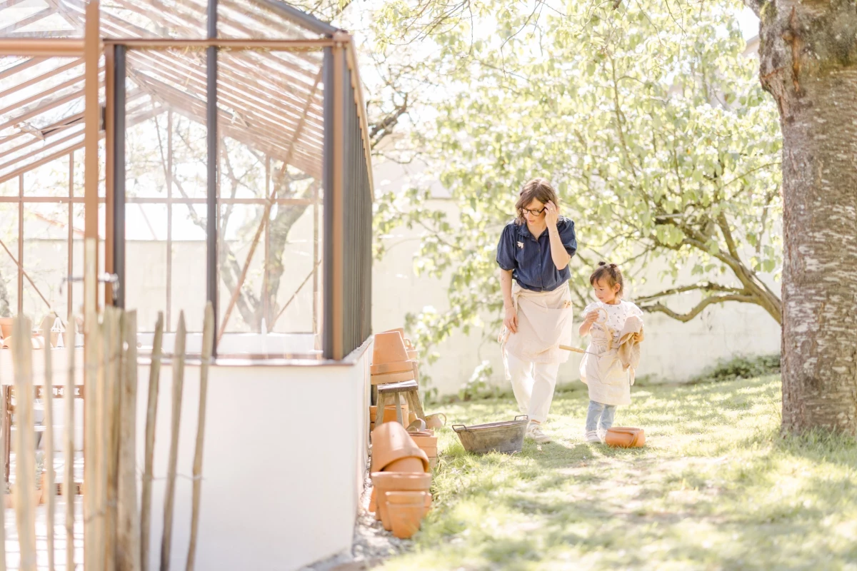 Séance famille en extérieur : maman court avec ses deux filles dans un jardin printanier, complicité et rires partagés