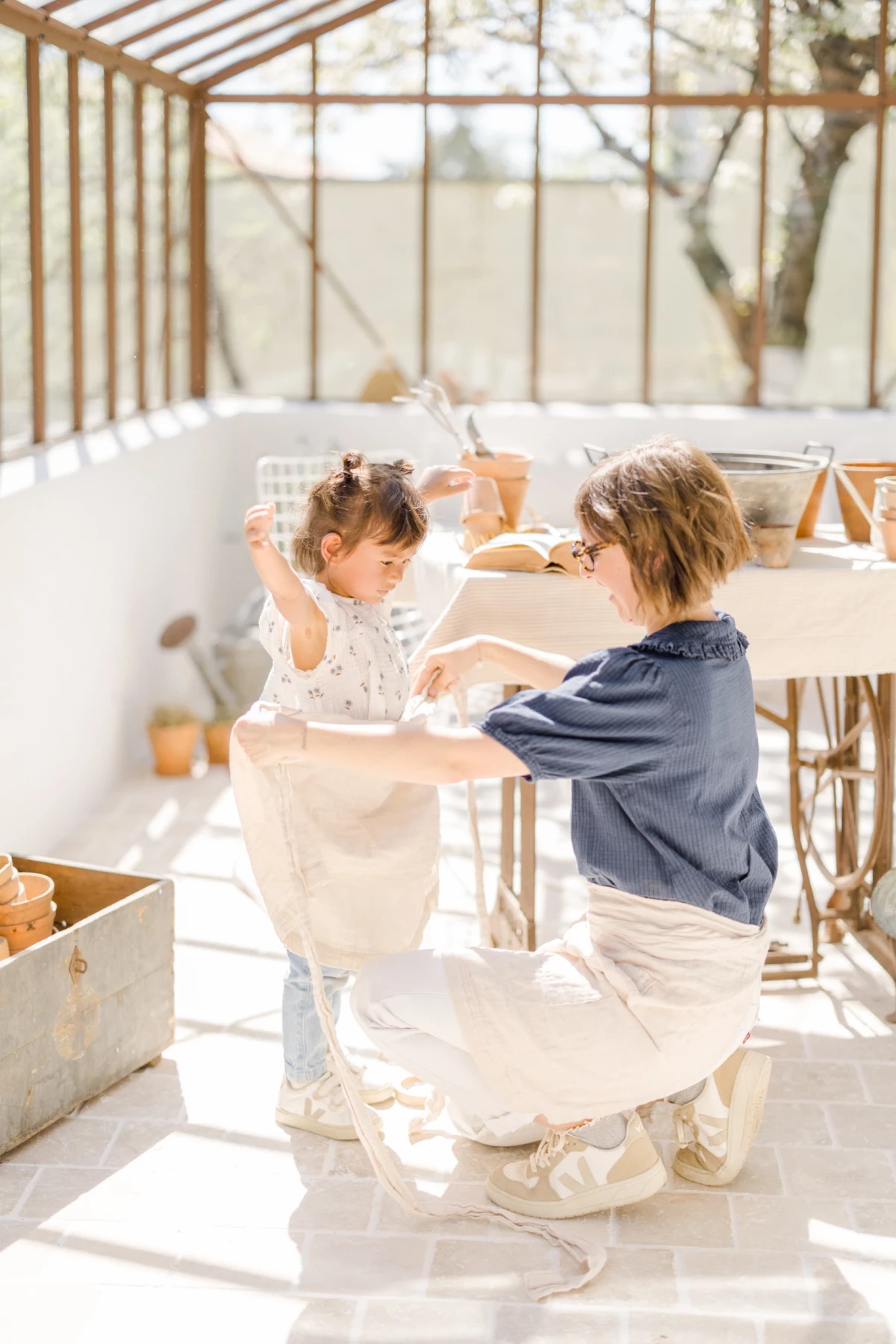 Séance famille printemps : mère et fille partagent un moment de complicité autour du jardinage dans une verrière lumineuse
