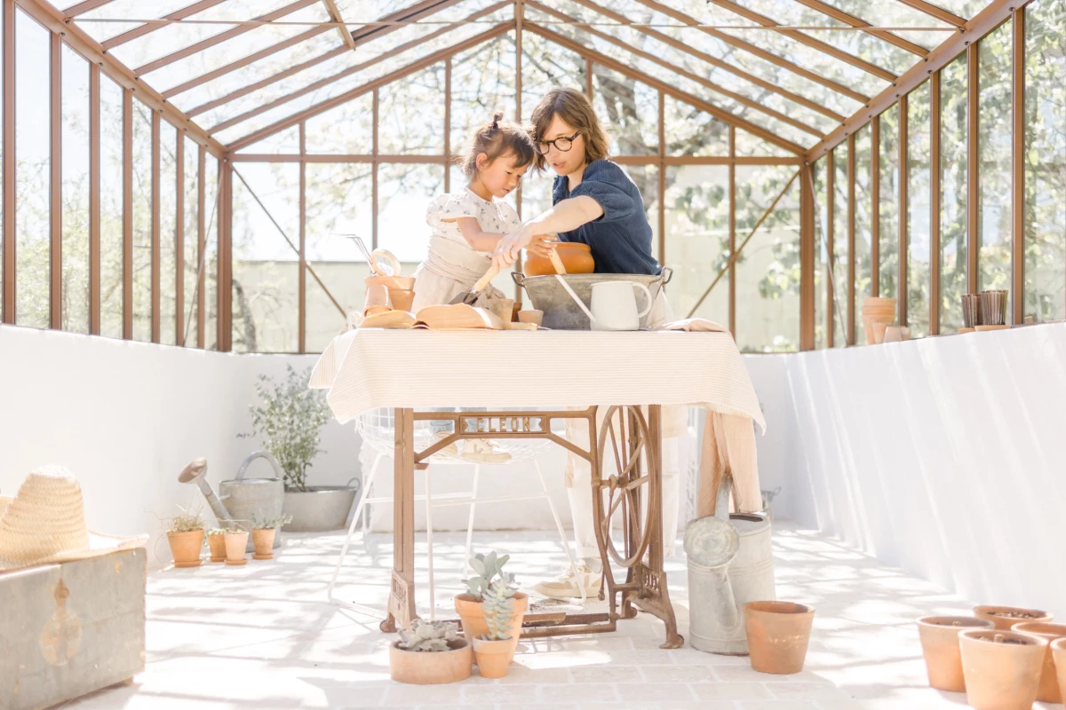 Séance famille printemps : mère et fille partagent un instant de complicité dans une serre lumineuse, ambiance douce et naturelle