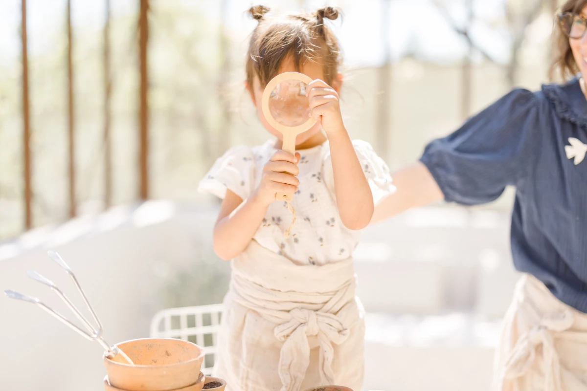 Séance photo famille : petite fille souriante découvre le jardinage avec sa maman dans une verrière lumineuse en Vendée