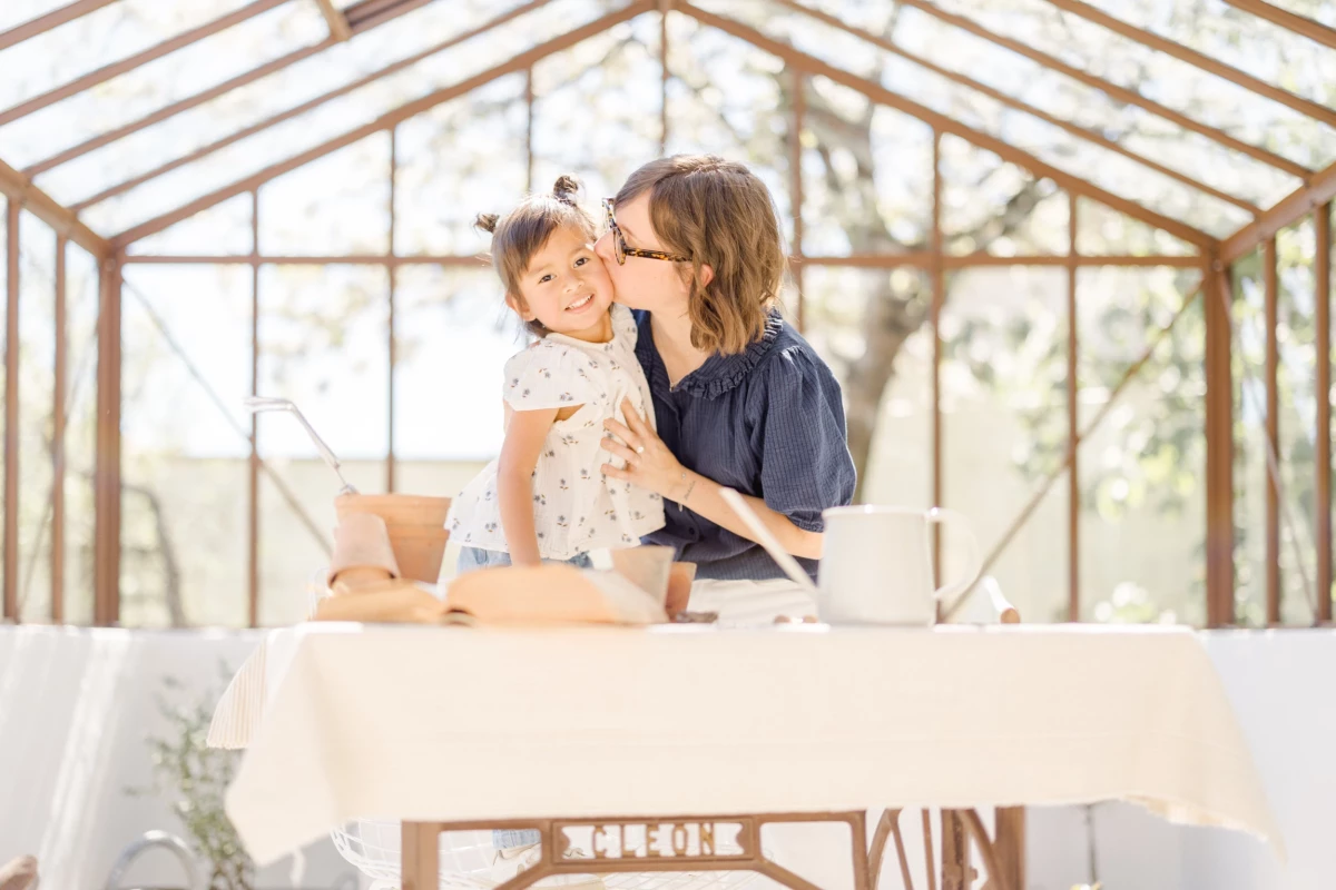 Séance famille en verrière : mère et fille partagent un moment de complicité et de tendresse dans une lumière naturelle printanière