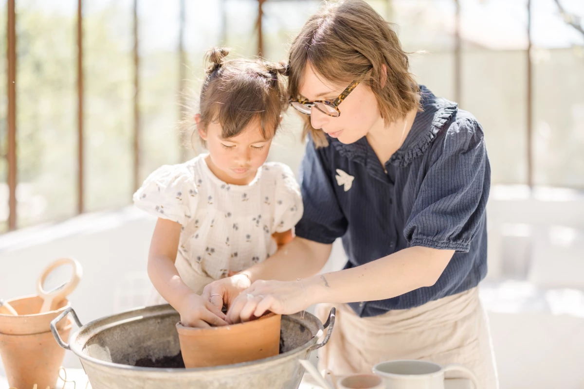Séance famille en verrière : mère et fille partagent un moment de complicité autour du jardinage dans une lumière de printemps