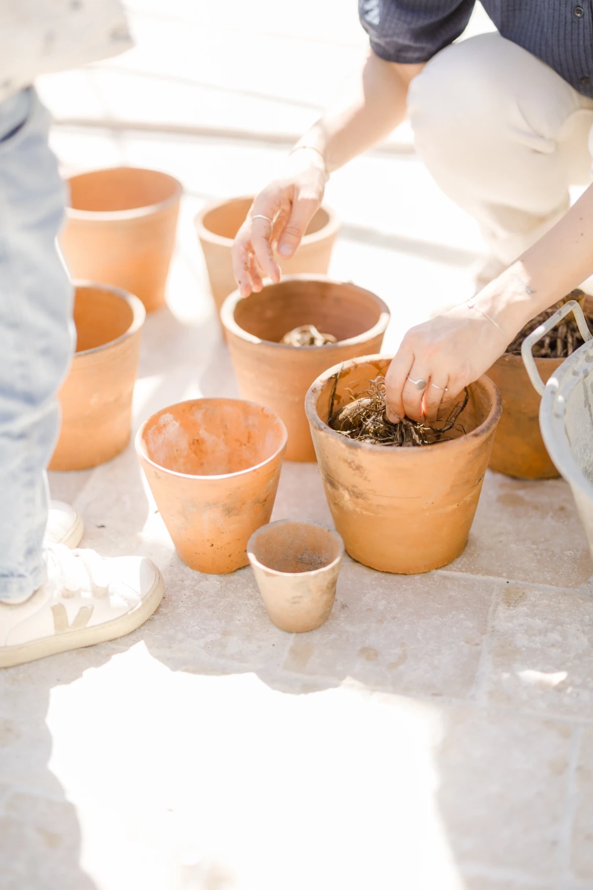 Séance famille au printemps : maman et fille jardinent ensemble dans des pots en terre cuite, moment de complicité naturelle