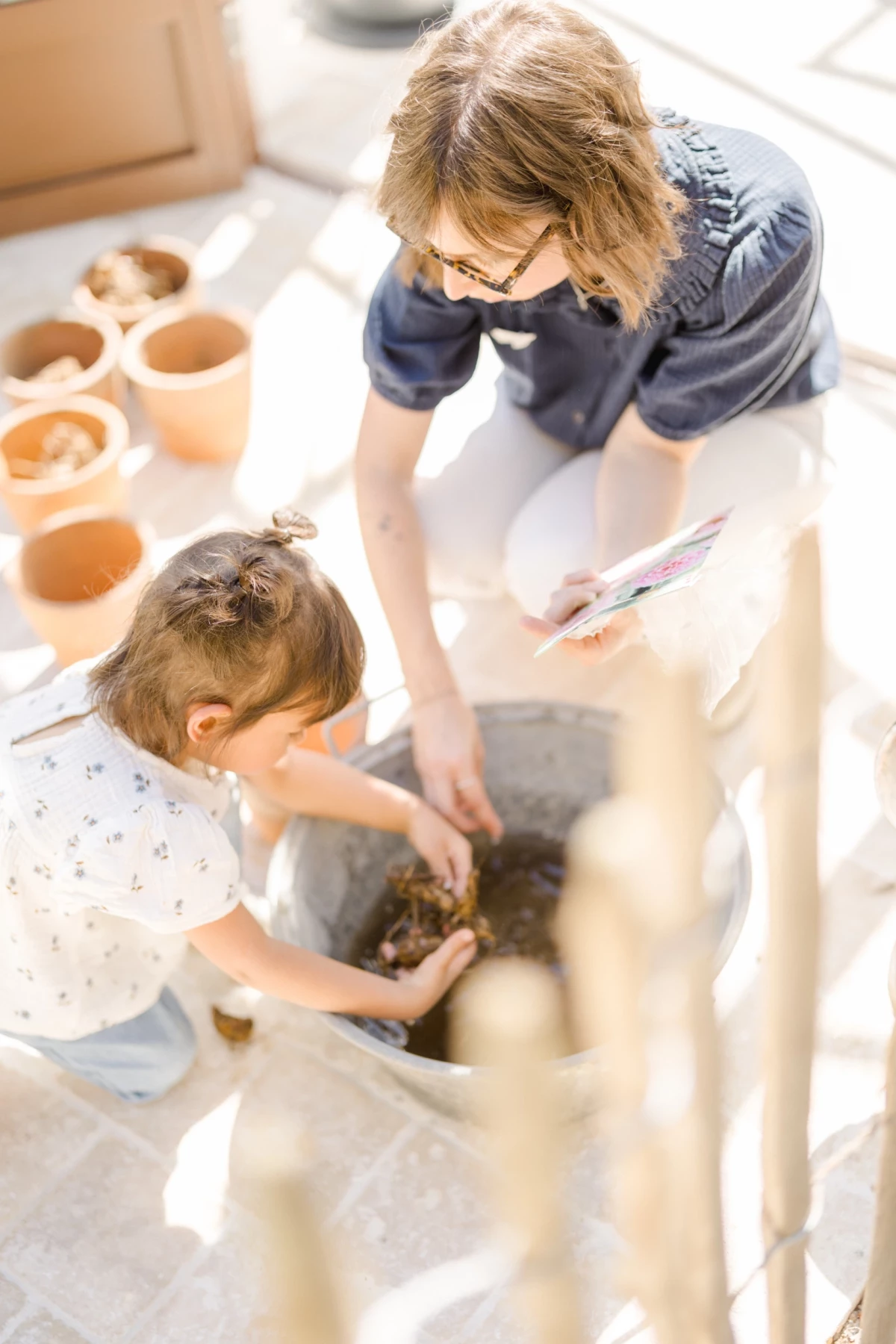 Séance famille studio : mère et fille jardinent ensemble, geste complice, lumière naturelle douce, moment de complicité printanier