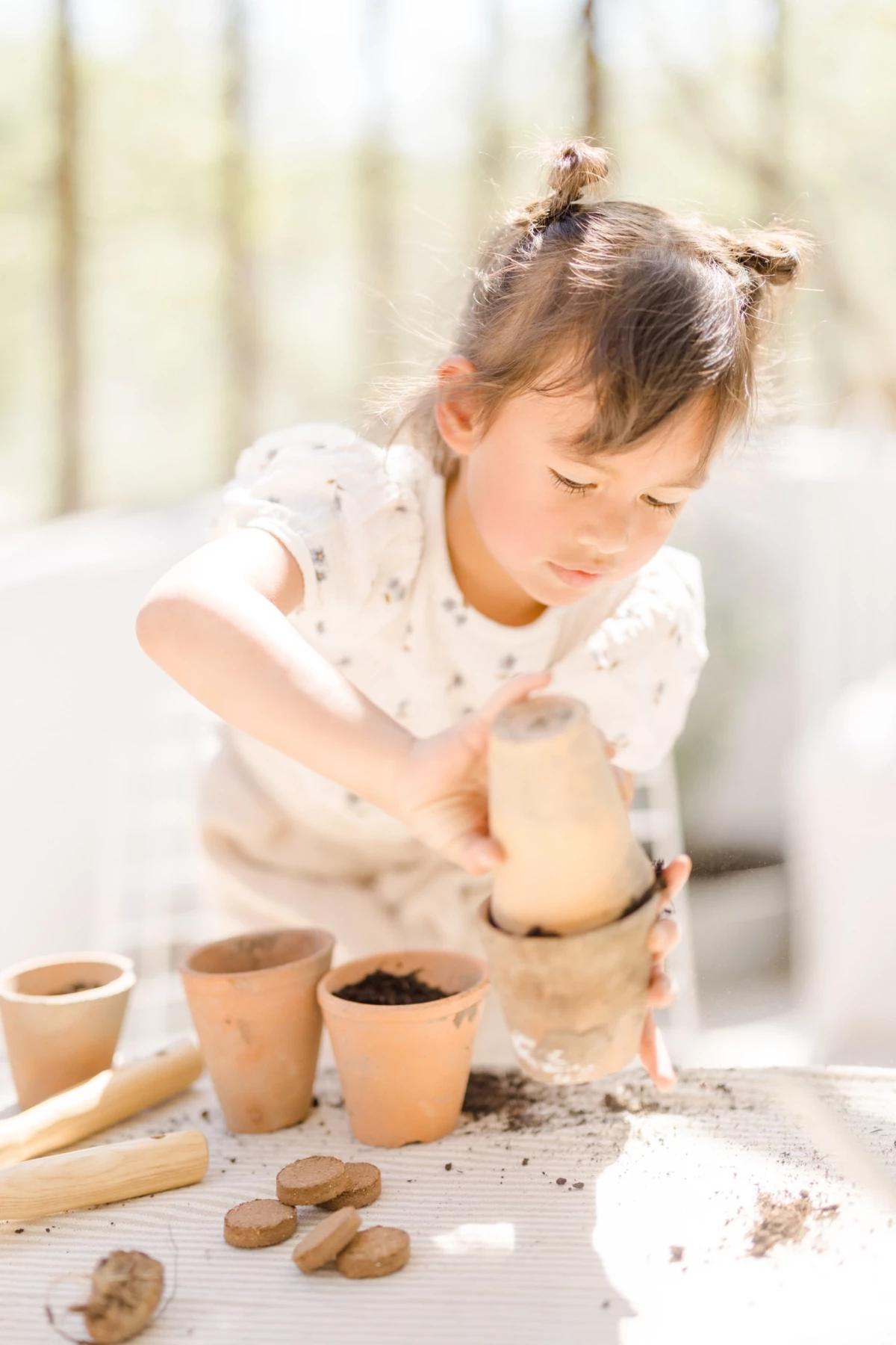 Séance famille en verrière : petite fille concentrée façonne l'argile avec ses mains, instant de créativité et de douceur printanière