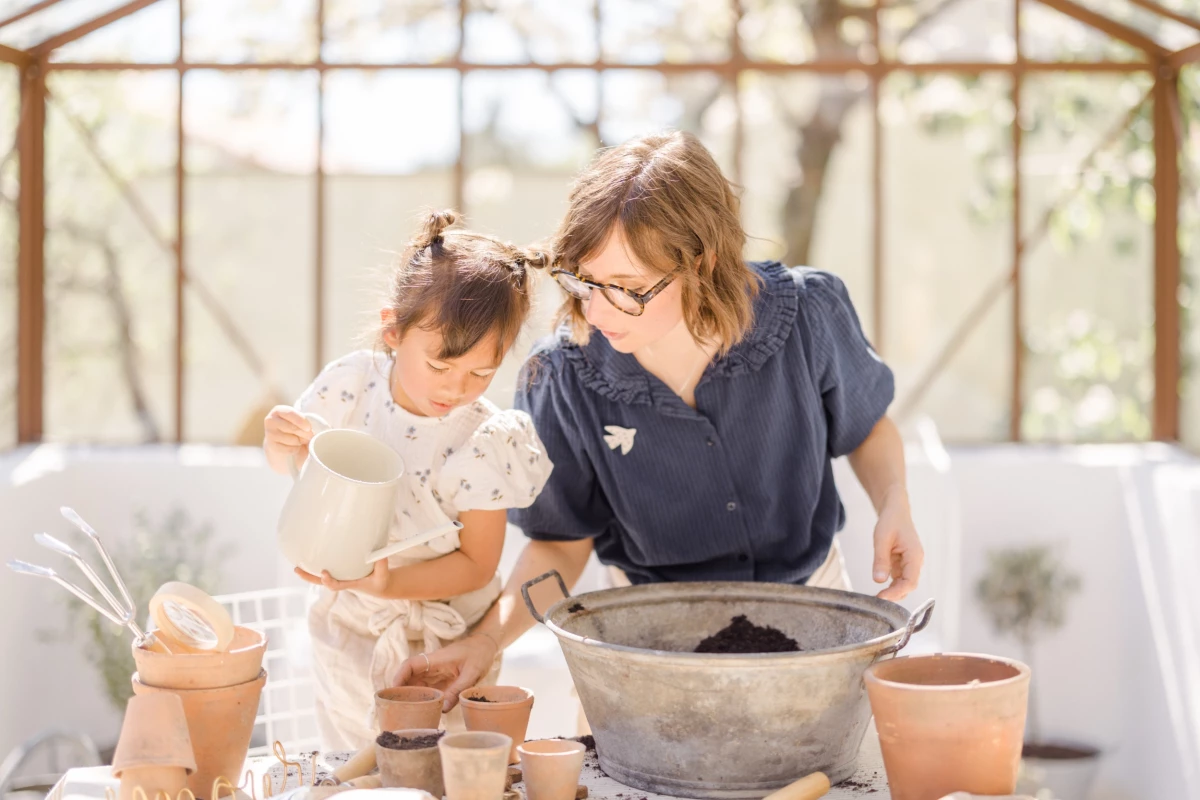Séance famille dans une verrière : mère et fille partagent un atelier jardinage complice au printemps, lumière douce et naturelle