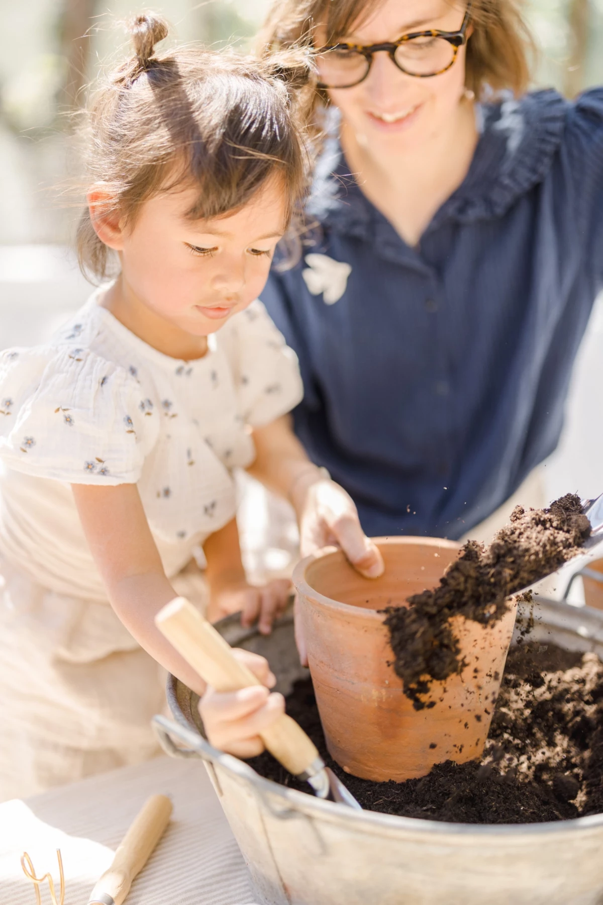 Séance famille printemps : mère et fille jardinent ensemble dans une verrière lumineuse, moment de complicité naturelle