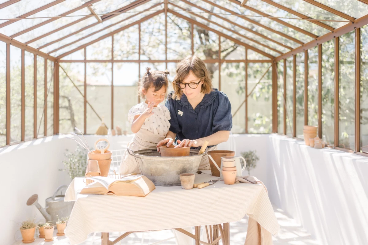 Séance famille en verrière : mère et fille partagent un moment de complicité autour du jardinage dans une lumière douce de printemps