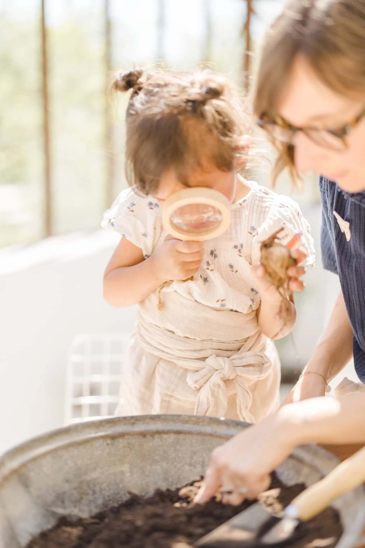 Séance famille Vendée : mère et fille jardinent ensemble dans une verrière, moment de complicité naturelle et authentique au printemps