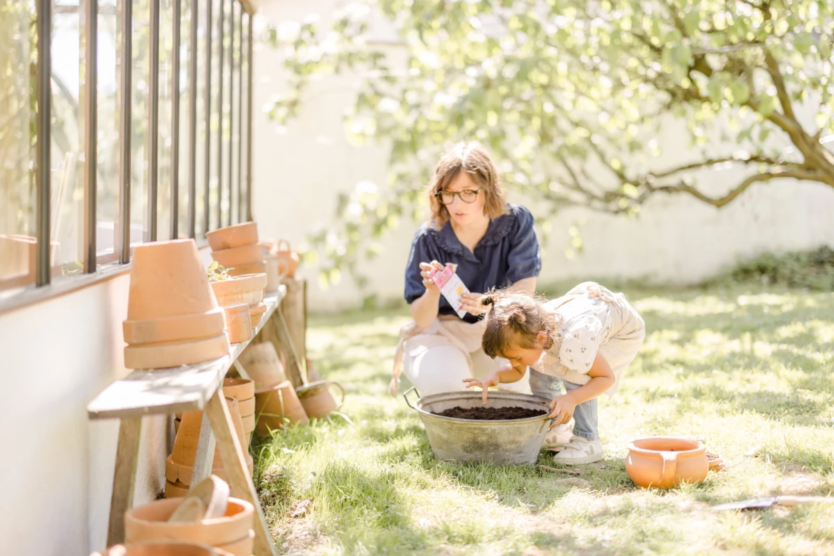 Séance famille en extérieur : mère et fille jardinent ensemble sous une verrière lumineuse, instant de complicité et douceur printanière