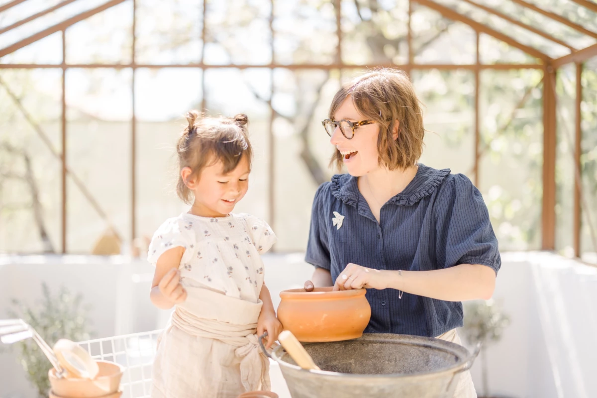 Séance famille en verrière : mère et fille partagent un moment de complicité autour d'une activité jardinage, lumière douce printanière