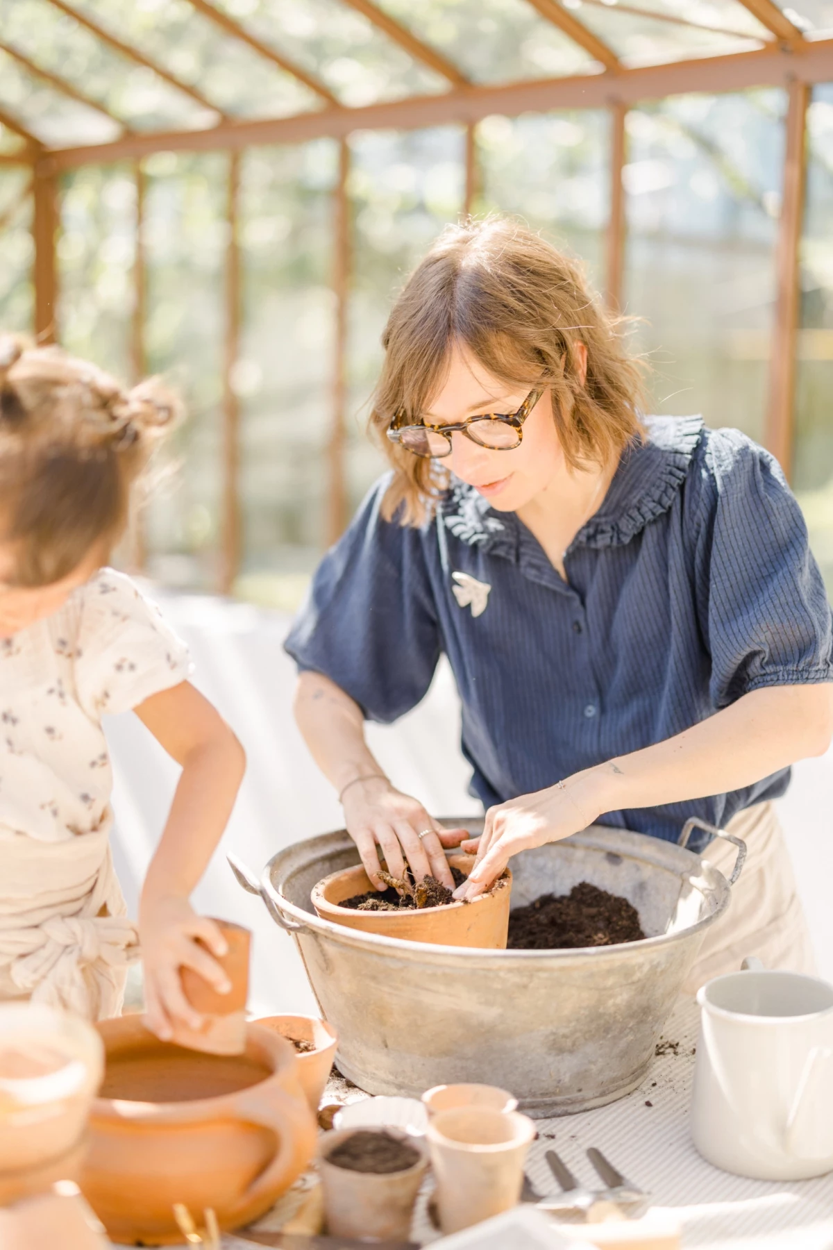 Séance famille en verrière : mère et fille partagent un moment de complicité autour d'une activité jardinage, lumière naturelle douce