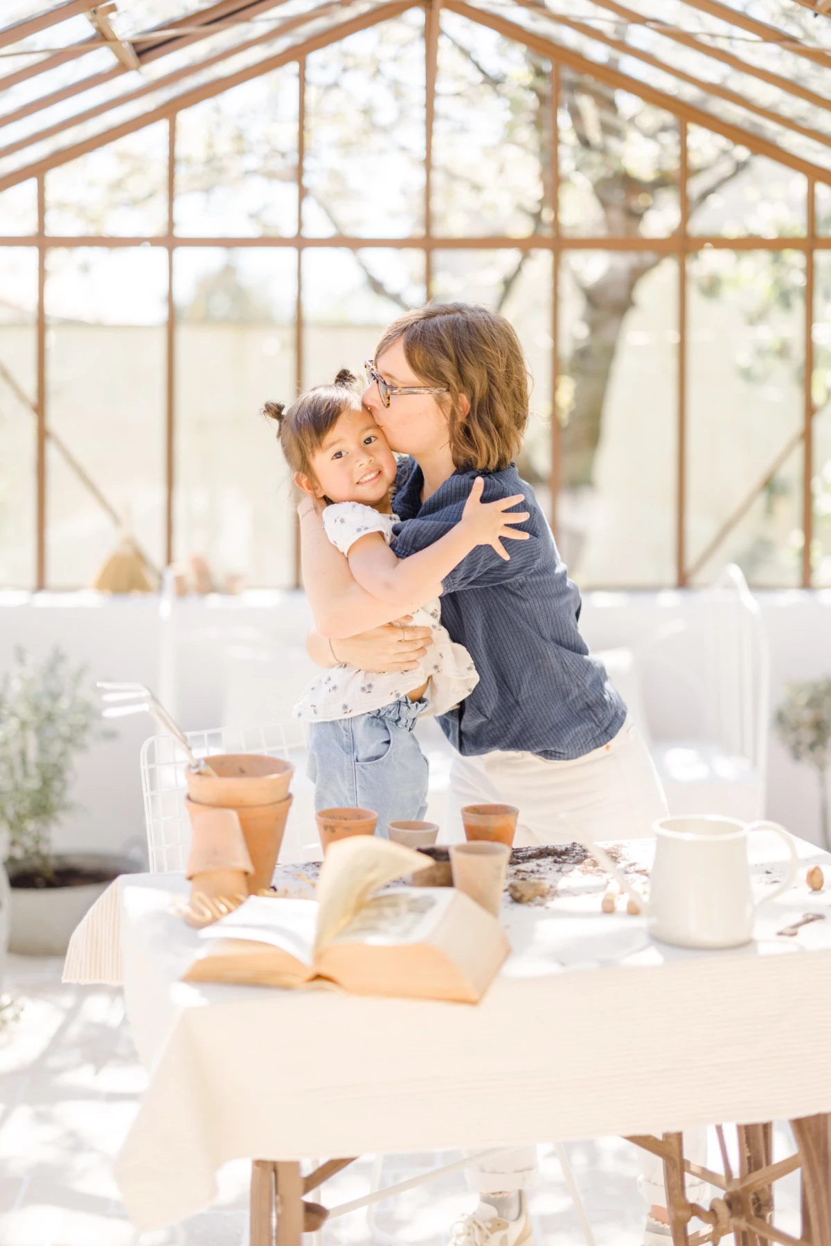 Séance photo famille : mère et fille s'enlacent tendrement dans une verrière lumineuse, moment complice lors d'un atelier jardinage