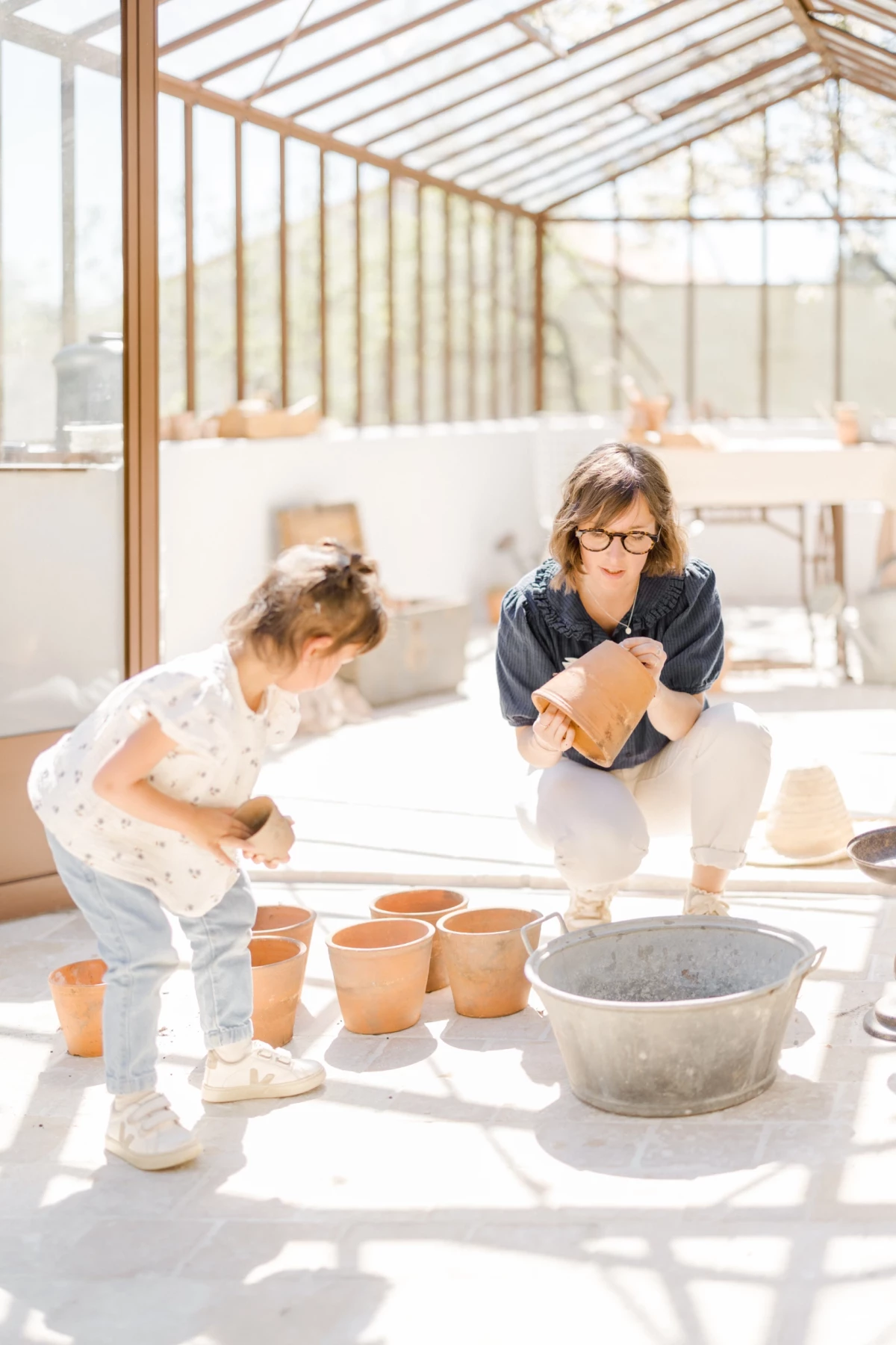 Séance famille en studio : mère et fille partagent un atelier poterie dans une verrière lumineuse, complicité et créativité
