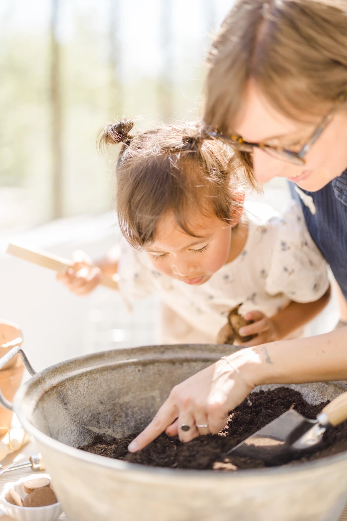 Séance famille printemps : mère et fille jardinent ensemble dans une verrière lumineuse, instant de complicité naturelle