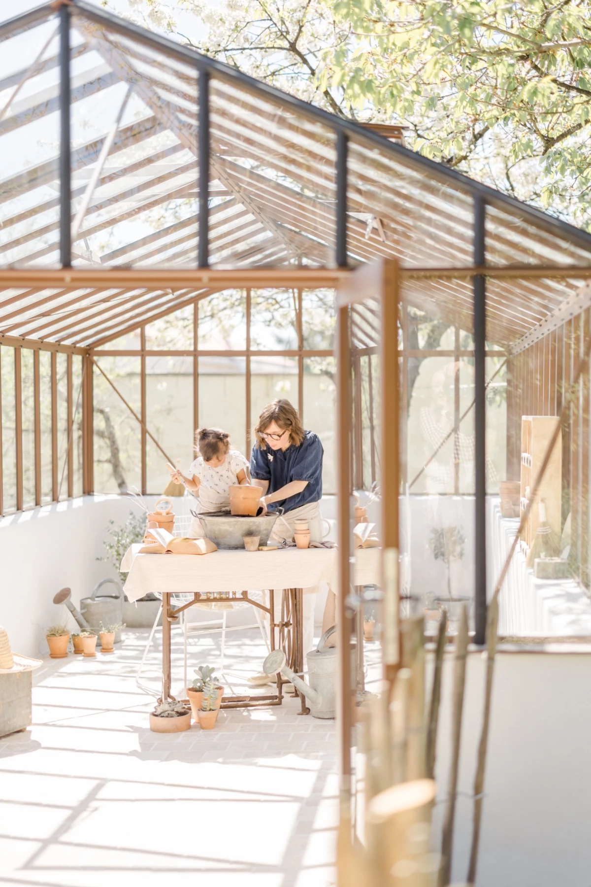 Séance famille printemps : mère et fille partagent un moment de complicité dans une verrière lumineuse, ambiance jardinage douce