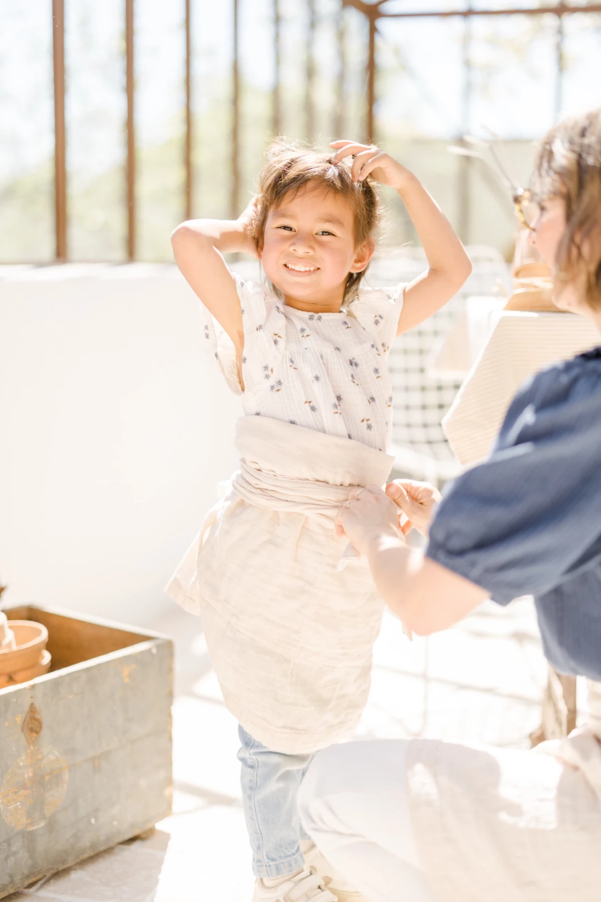 Séance famille printemps : fillette souriante jardine avec sa mère dans une verrière lumineuse, moment de complicité naturelle