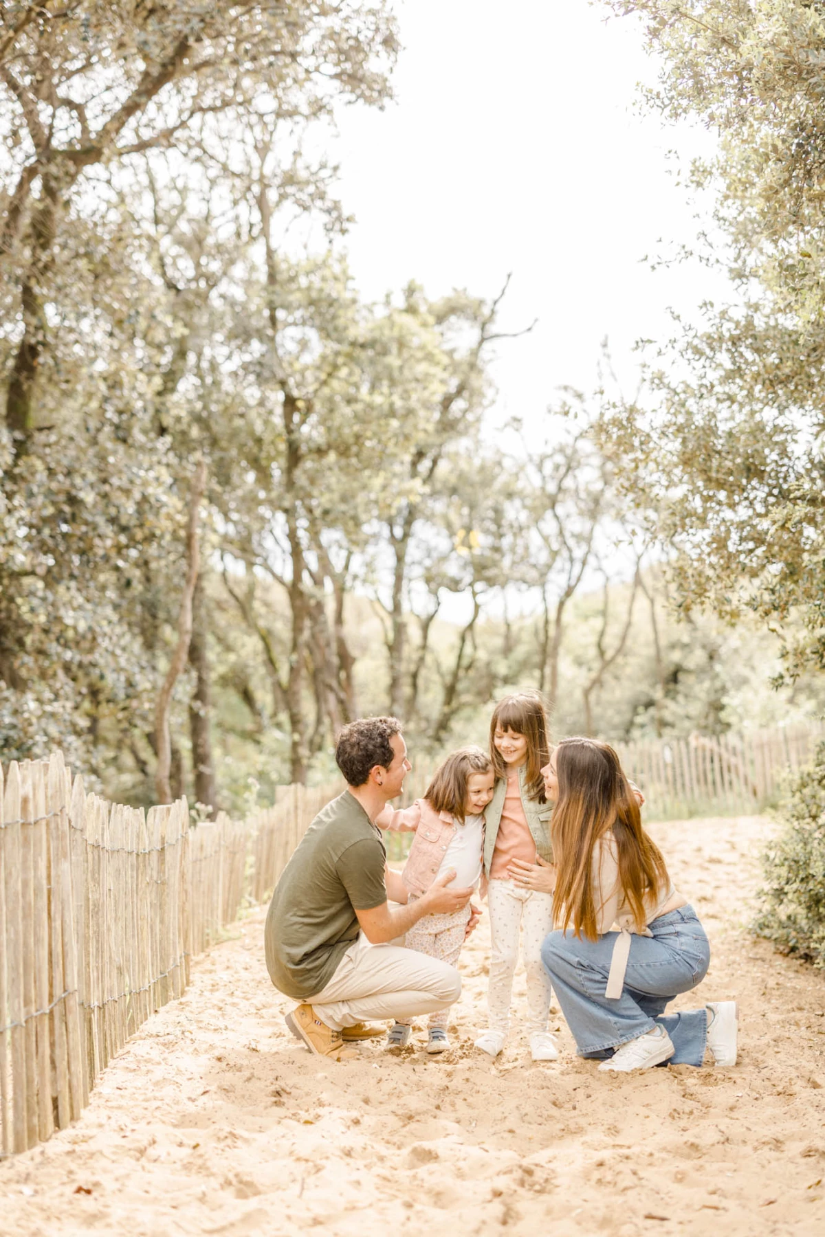 Séance famille en extérieur : parents et deux enfants partagent un moment de complicité sur le sable dans une lumière douce et naturelle
