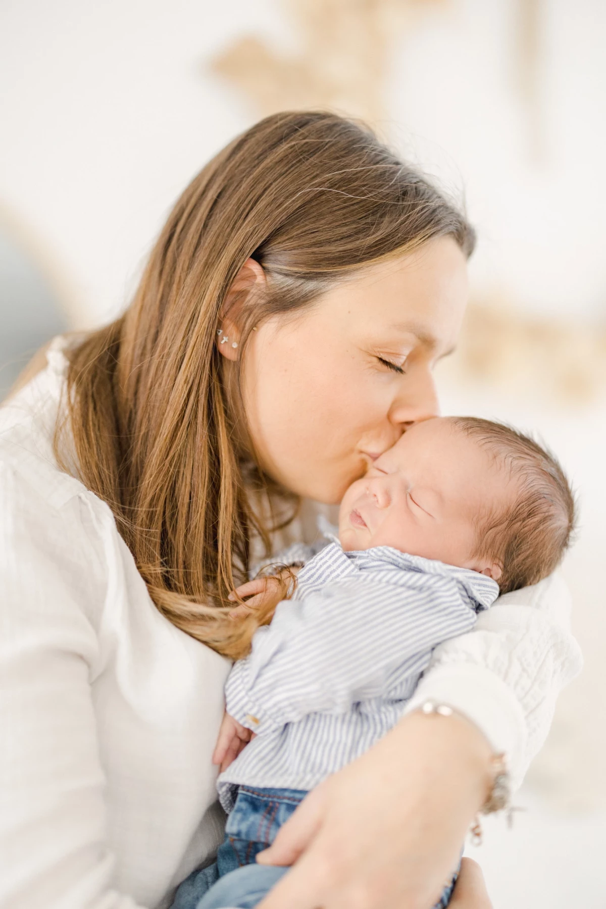 Séance naissance au studio : maman embrasse tendrement son nouveau-né dans ses bras, moment de douceur et d'amour maternel en Vendée