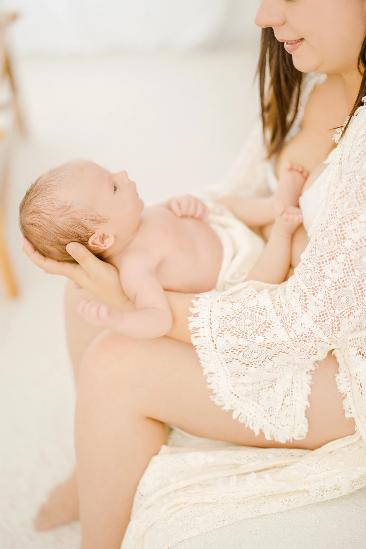 Séance allaitement au studio : maman berce son nouveau-né peau à peau dans une lumière naturelle douce et épurée en Vendée