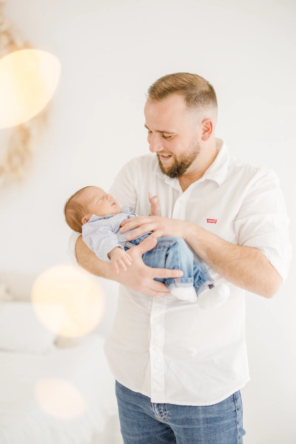 Séance naissance en studio : jeune papa berce son nouveau-né avec tendresse dans une lumière douce et épurée