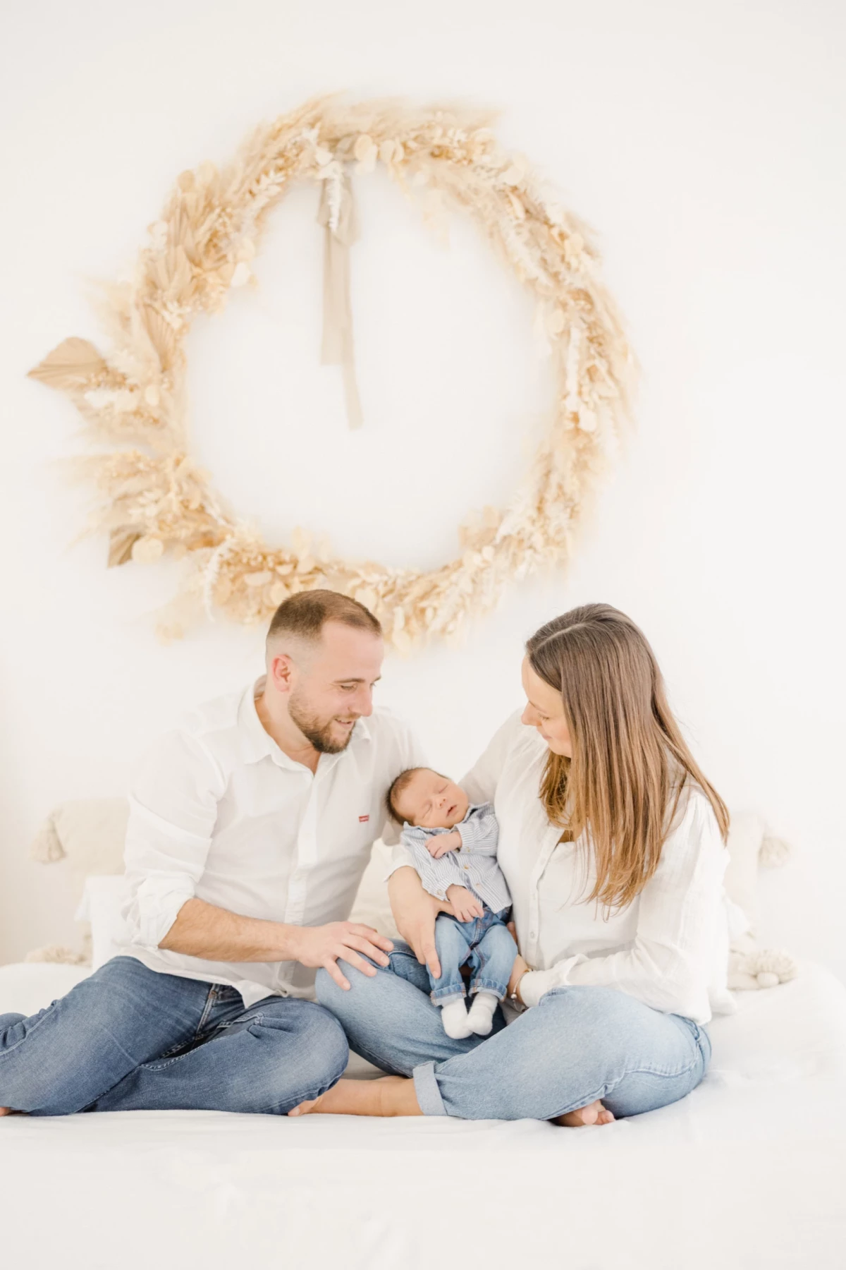 Séance naissance en studio : parents assis en tailleur avec leur nouveau-né, ambiance douce et lumineuse sur tons beige et blanc