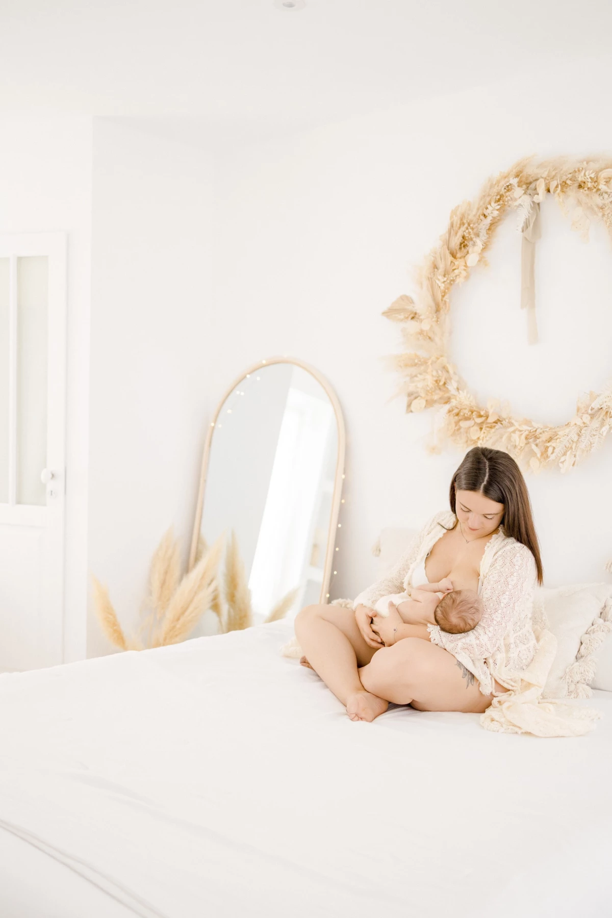 Séance allaitement en studio : maman allaitant son nouveau-né sur un lit blanc, lumière naturelle et douceur maternelle en Vendée