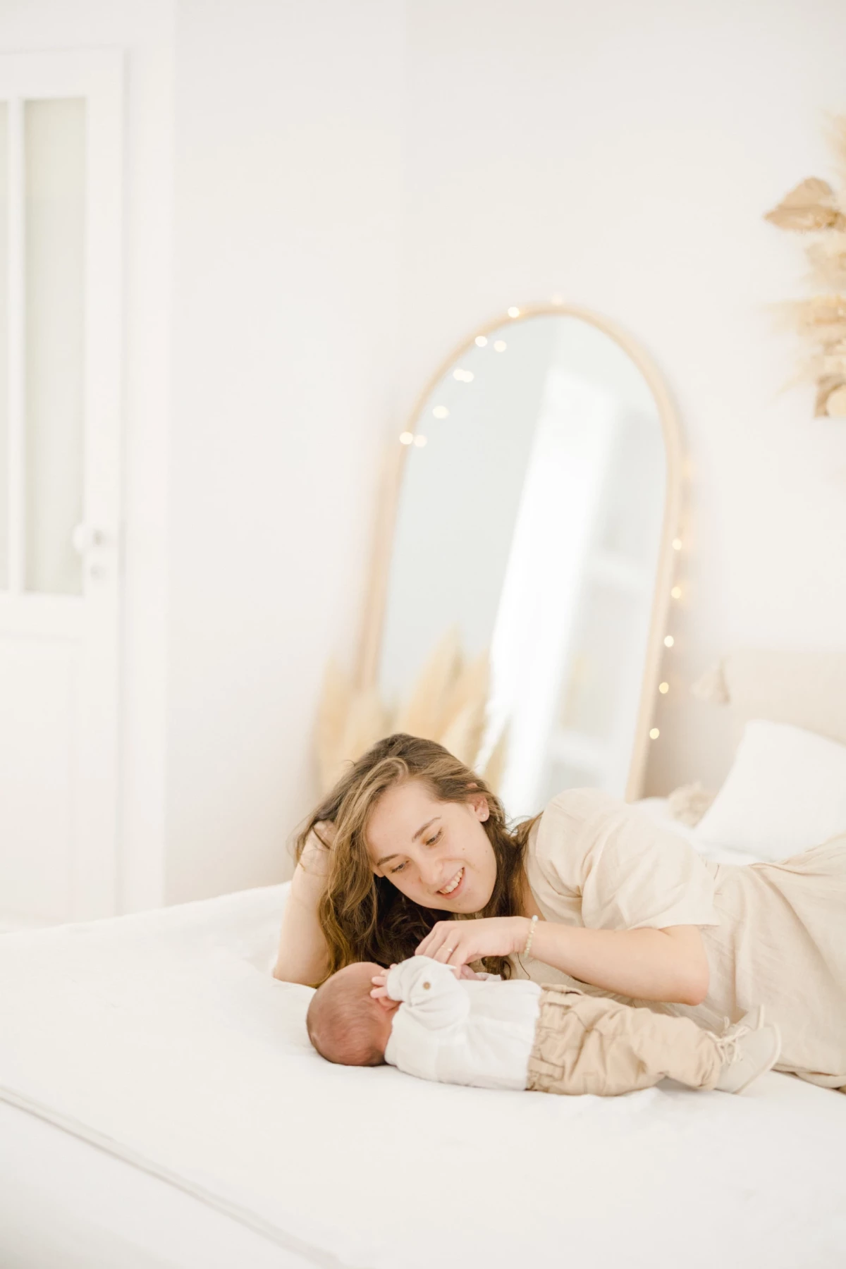 Séance nouveau-né en studio : maman allongée contemple son bébé avec tendresse dans une ambiance lumineuse et douce