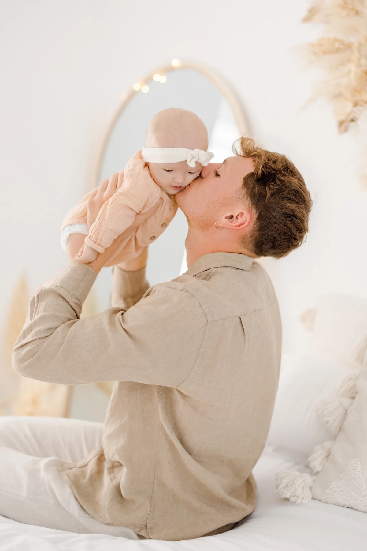 Séance naissance en studio : papa embrasse tendrement sa petite fille de 4 mois dans une lumière douce et épurée