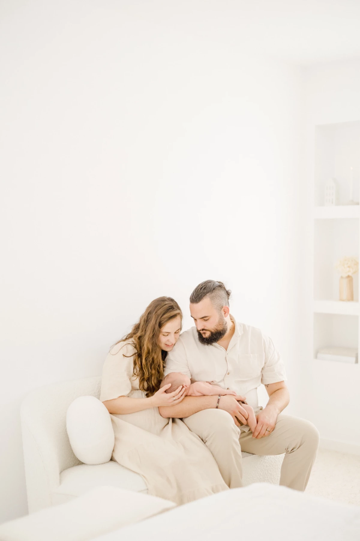 Séance naissance en studio : jeunes parents enlacent leur nouveau-né dans une atmosphère de tendresse et lumière douce
