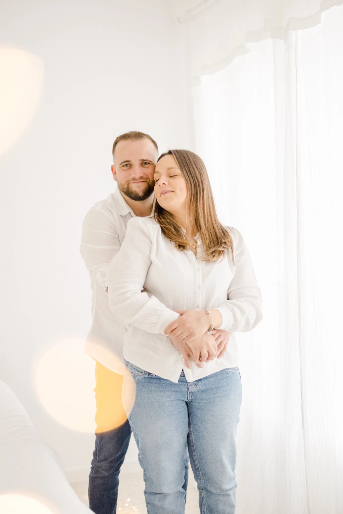 Séance naissance au studio : couple enlacé partage un instant de tendresse dans une lumière douce et épurée, ambiance beige et blanc