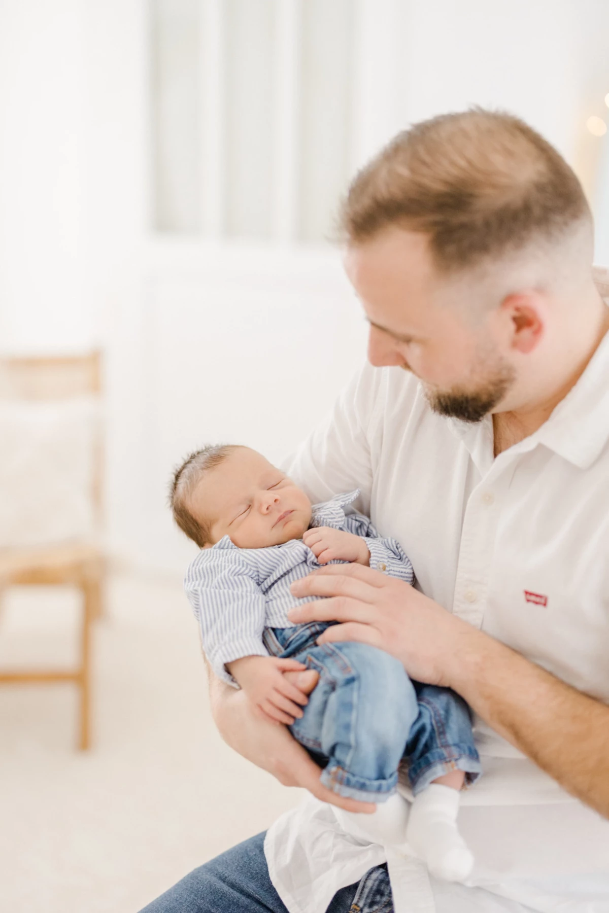 Séance naissance en studio : père berce son nouveau-né endormi dans ses bras, moment de tendresse et douceur paternelle en Vendée