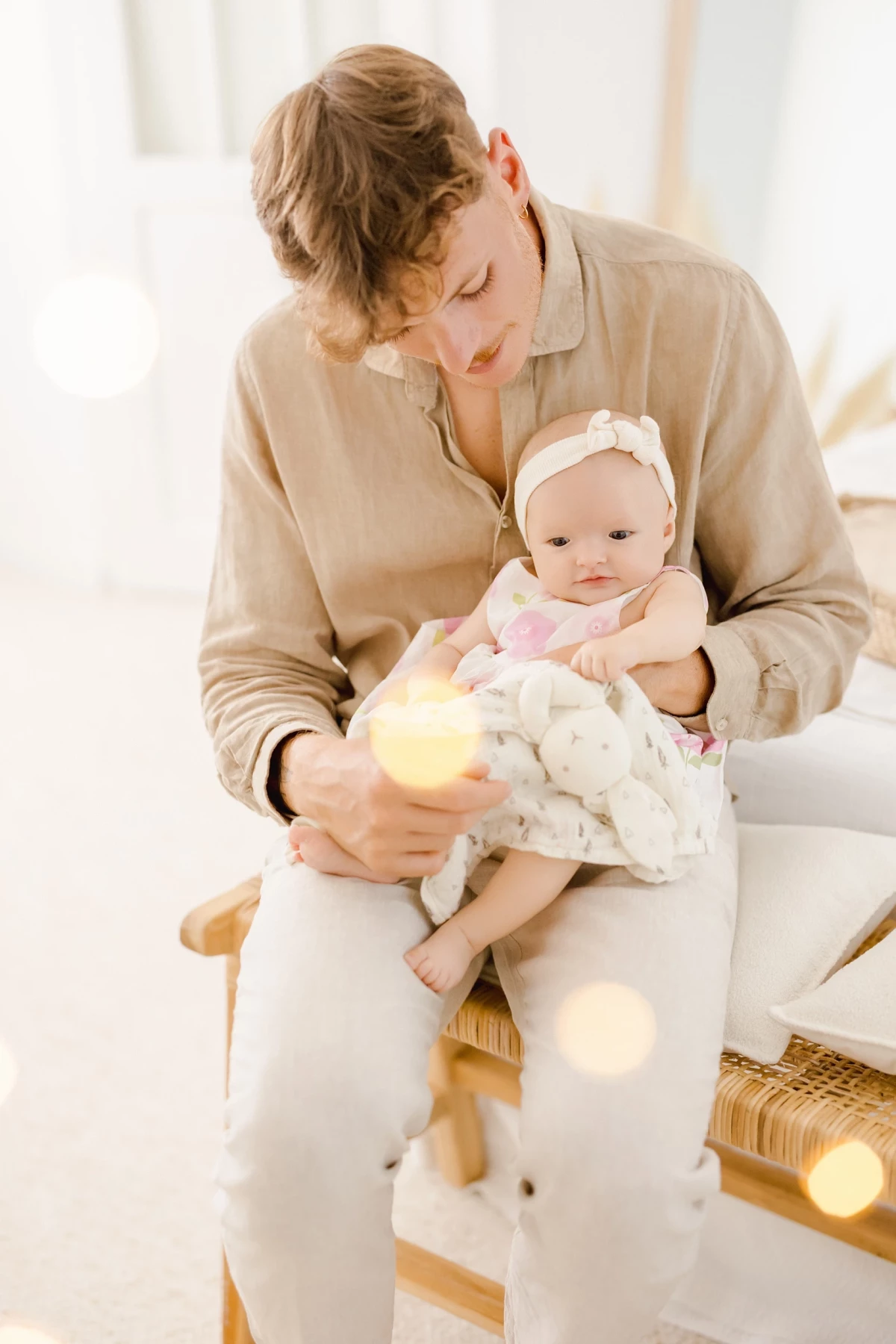 Séance naissance en studio : maman berce tendrement son bébé de 4 mois dans une ambiance douce et lumineuse en tons beige et blanc.