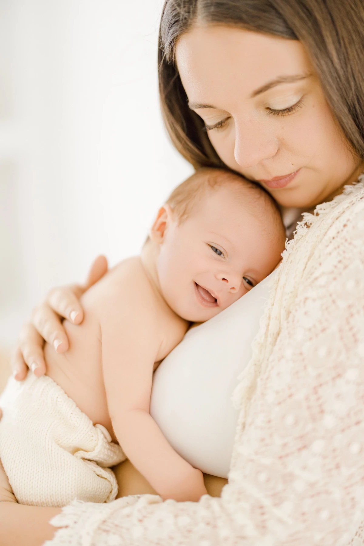 Séance naissance en studio : maman câline son nouveau-né en peau à peau, instant de tendresse et douceur maternelle dans la lumière naturelle