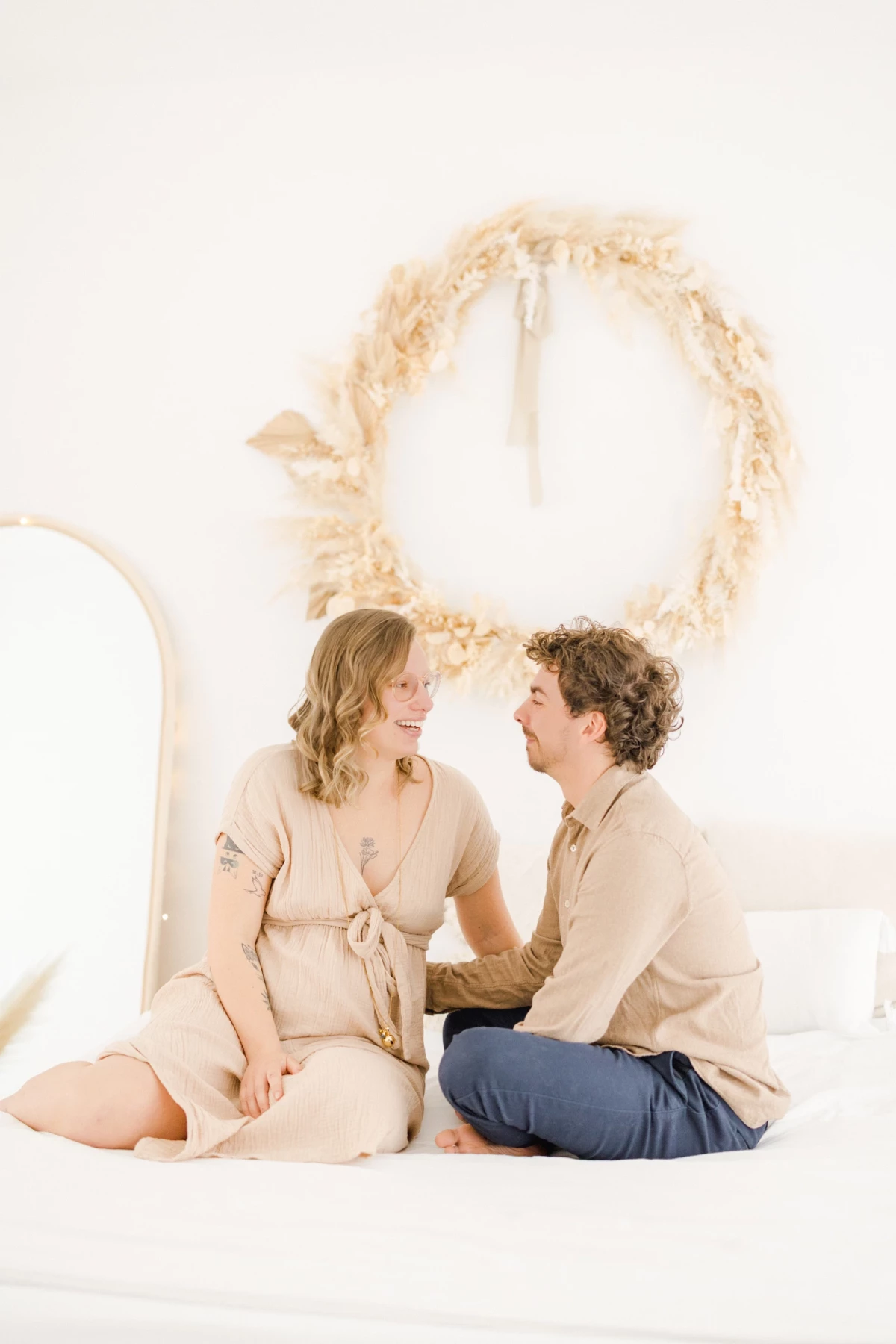 Séance grossesse en studio : couple complice échangeant un regard tendre dans une ambiance épurée aux tons beige et blanc
