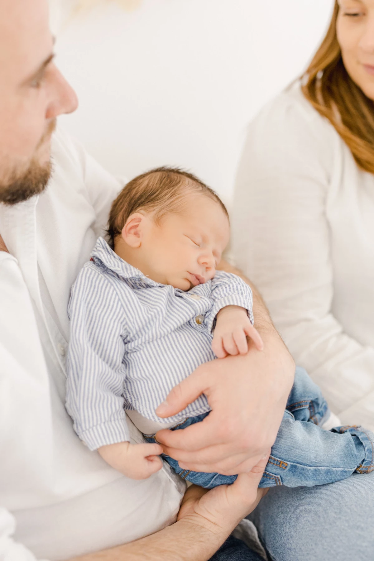 Séance naissance en studio : nouveau-né endormi dans les bras de son papa, entouré de sa famille dans une ambiance de tendresse