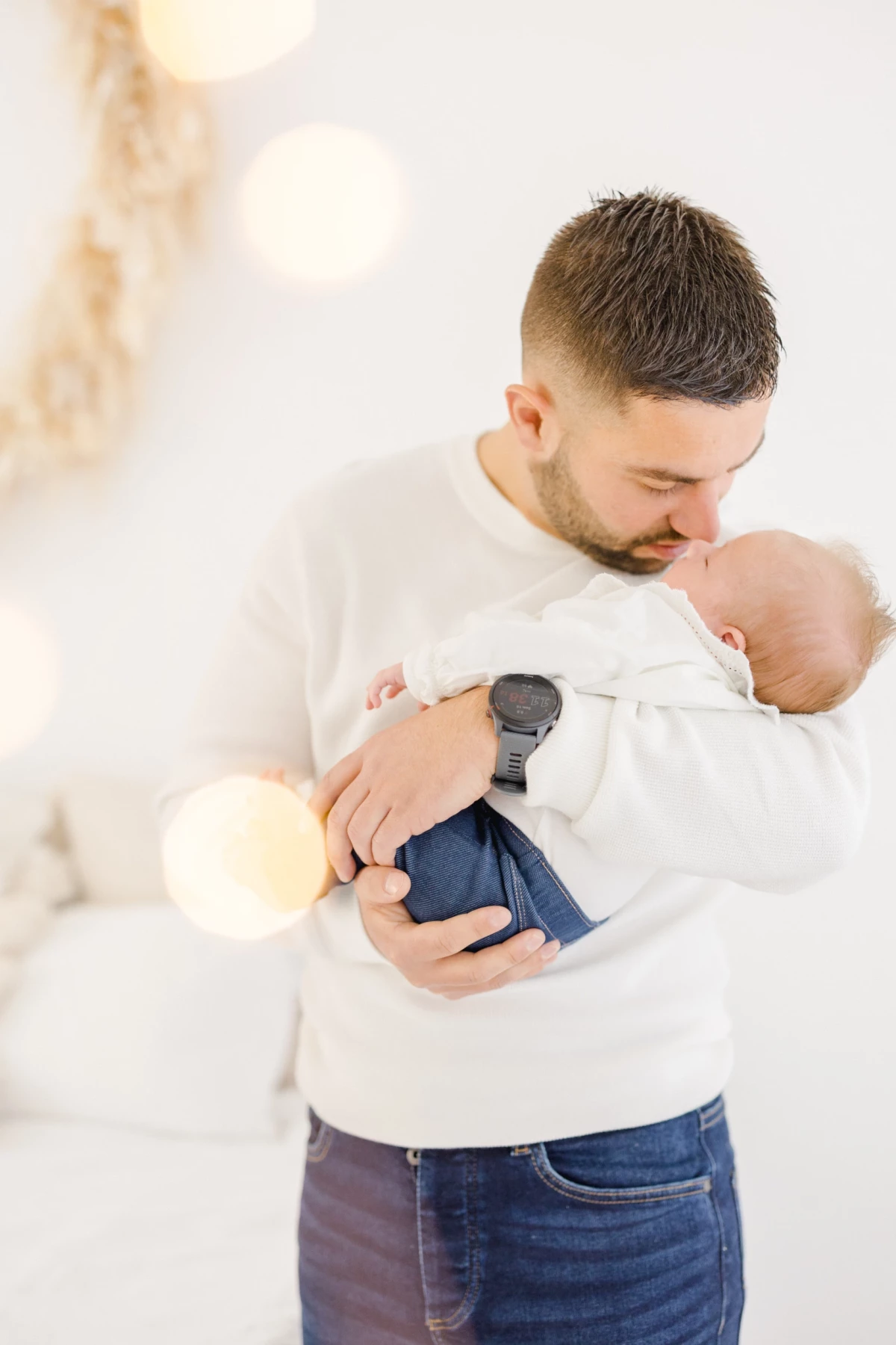 Séance naissance en studio : jeune papa câline son nouveau-né dans les bras, moment de tendresse et complicité paternelle