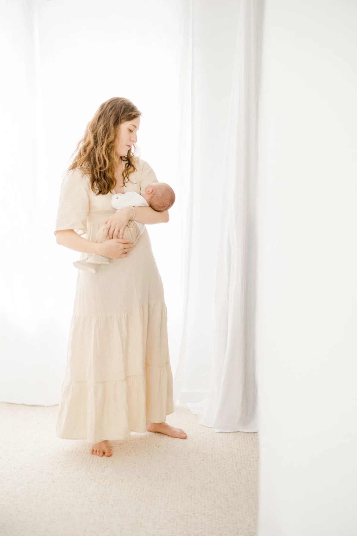 Séance nouveau-né au studio : maman allaite son bébé dans une robe beige, lumière douce et intimité maternelle en Vendée