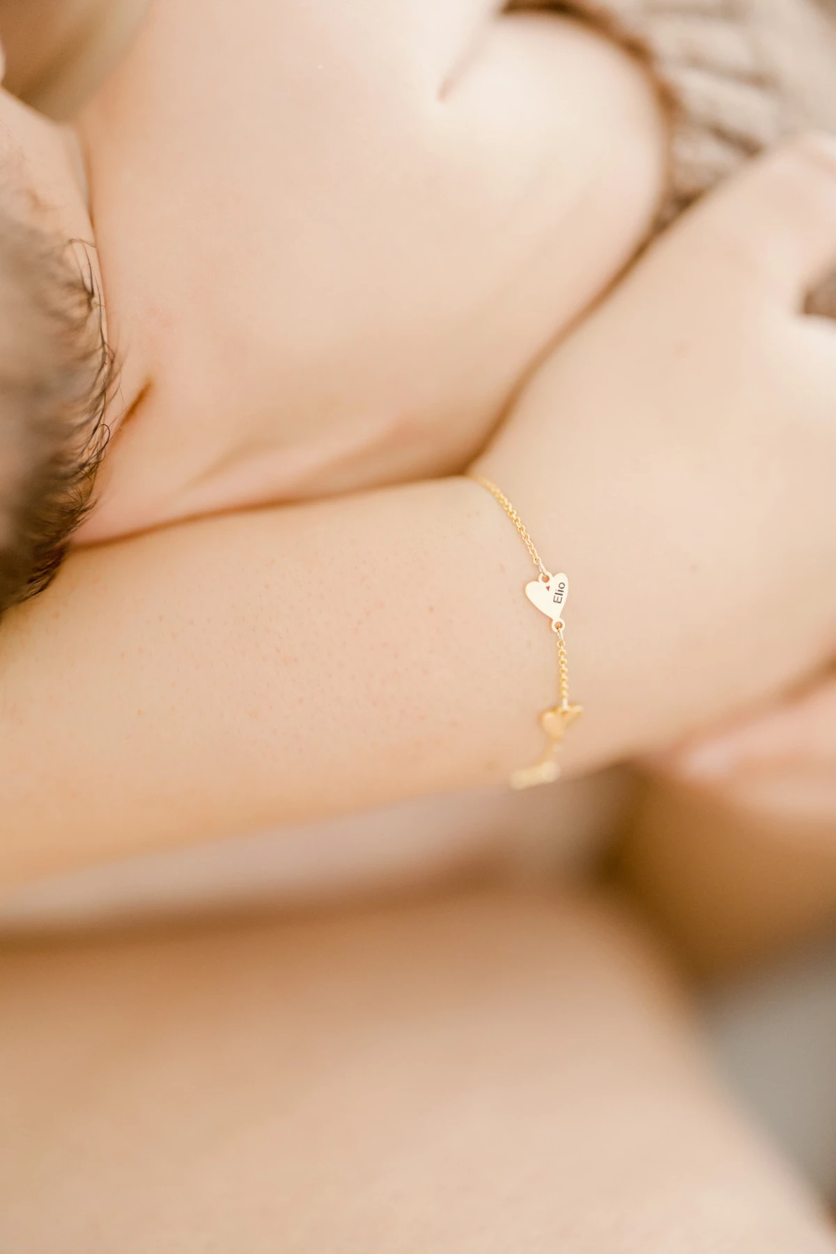 Séance naissance en studio : maman allaite son nouveau-né en douceur, bracelet doré délicat, lumière naturelle et intimité maternelle