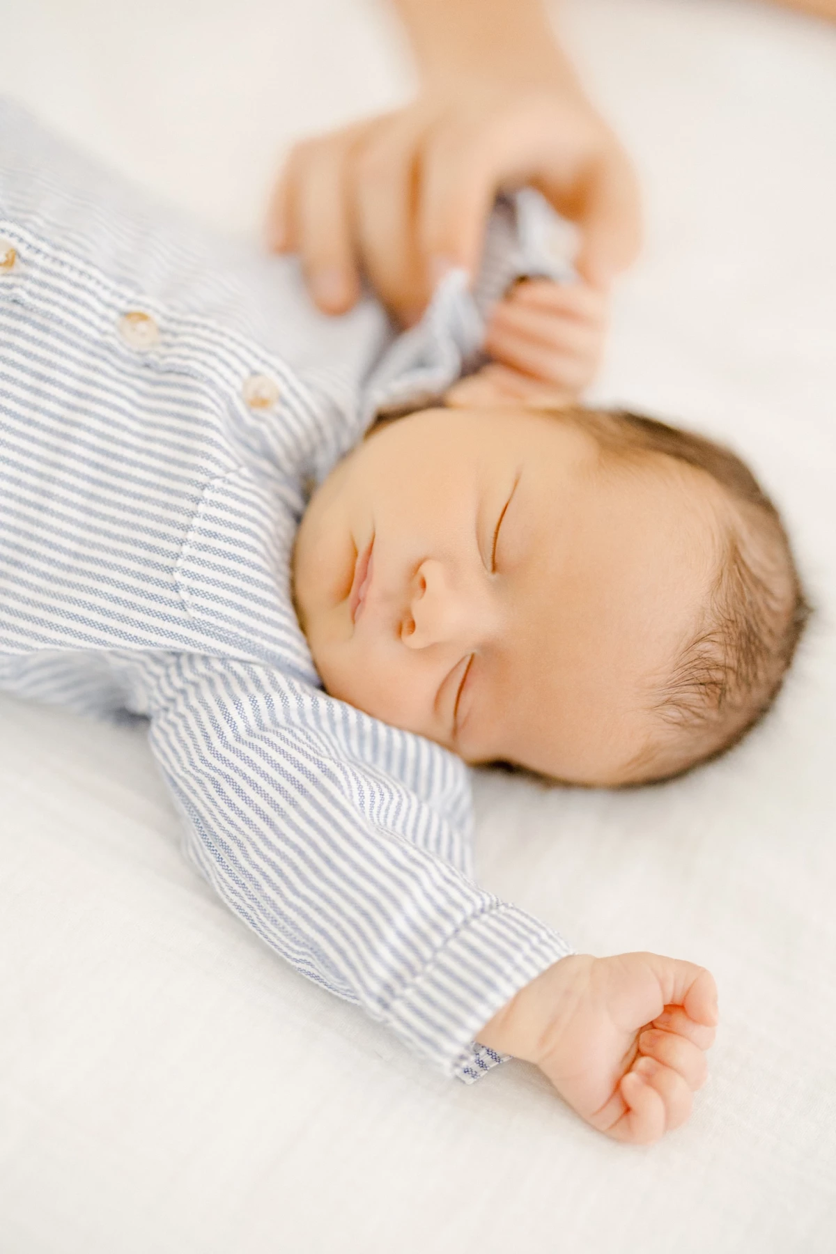 Séance nouveau-né en studio : bébé endormi en body rayé gris, expression sereine de tendresse, instant précieux immortalisé