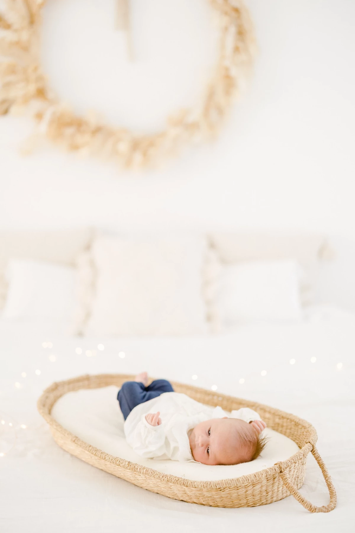 Séance naissance au studio : nouveau-né endormi dans un couffin en osier, enveloppé dans une couverture immaculée