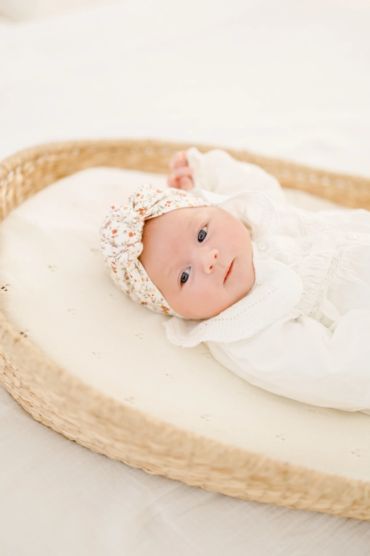 Séance naissance en studio : nouveau-né emmailloté dans un bonnet fleuri repose paisiblement dans un panier en osier naturel