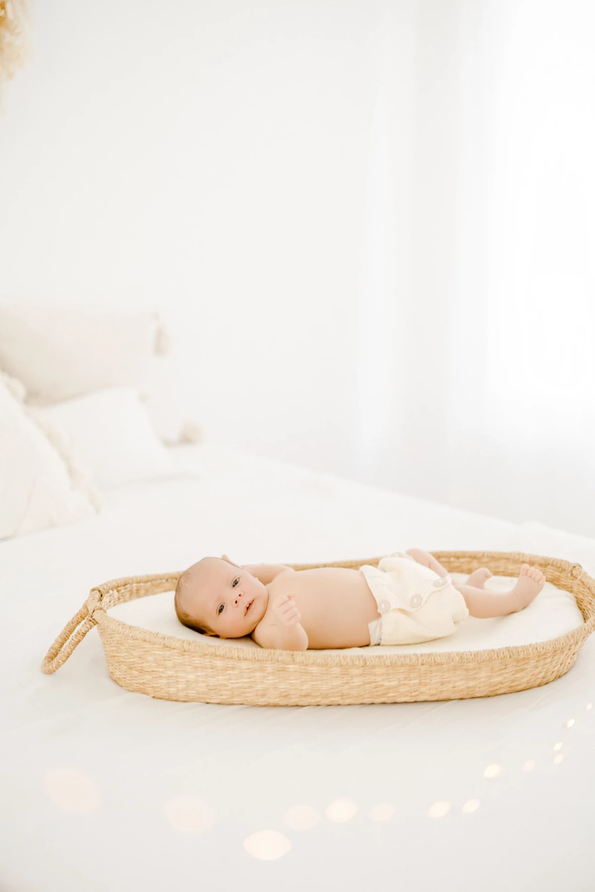 Séance nouveau-né au studio : bébé paisible allongé dans un couffin en osier, lumière naturelle douce et ambiance épurée