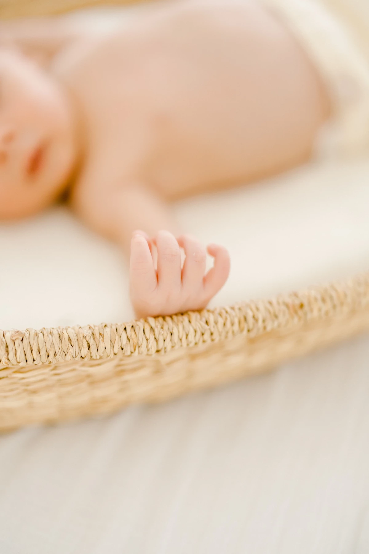 Séance nouveau-né au studio : petite main délicate d'un bébé posée sur un panier en osier, lumière douce et naturelle, tendresse