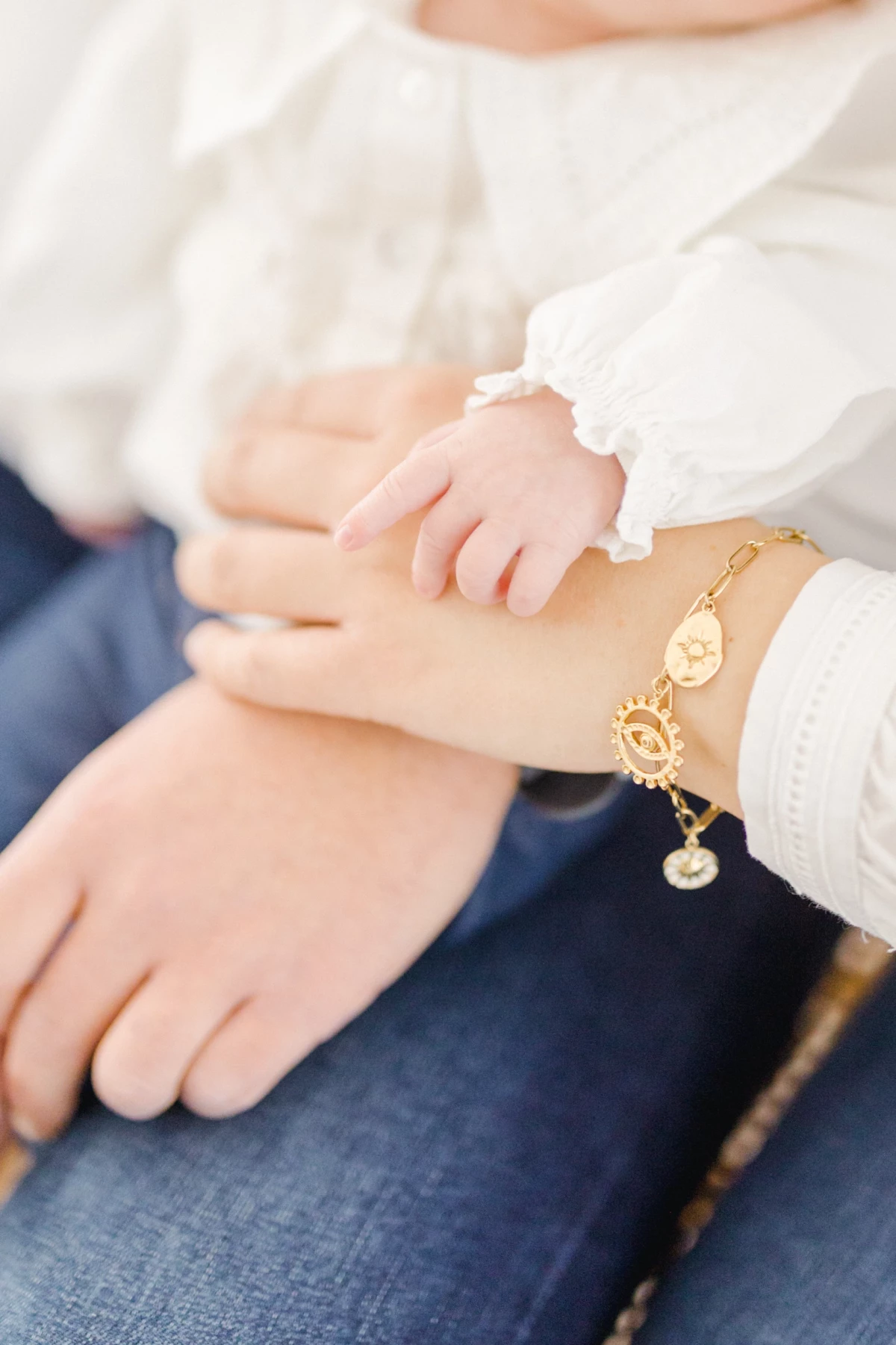 Séance nouveau-né en studio : mains de la maman et de bébé se rejoignent dans un geste de tendresse infinie et douceur maternelle
