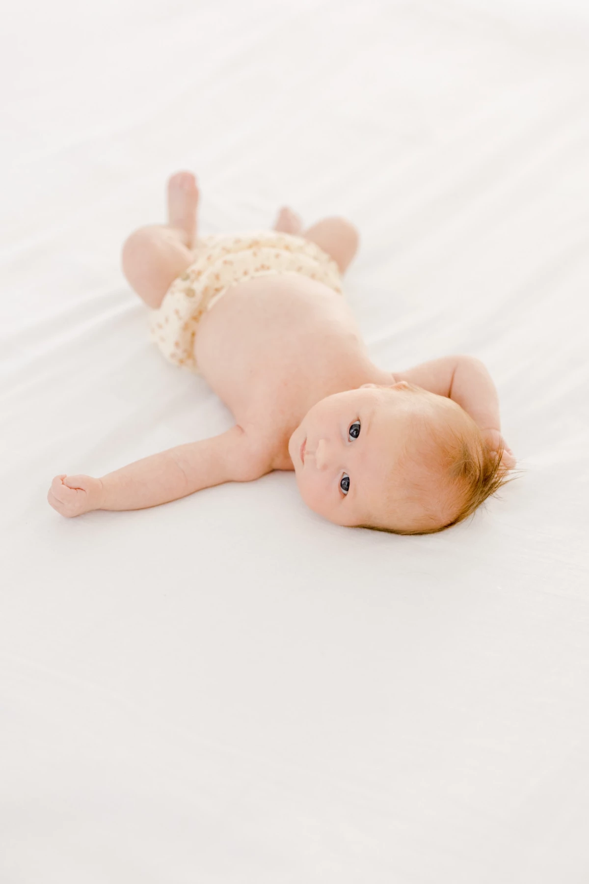 Séance nouveau-né au studio : bébé allongé paisiblement dans une tenue beige, instant de douceur et sérénité sur fond blanc